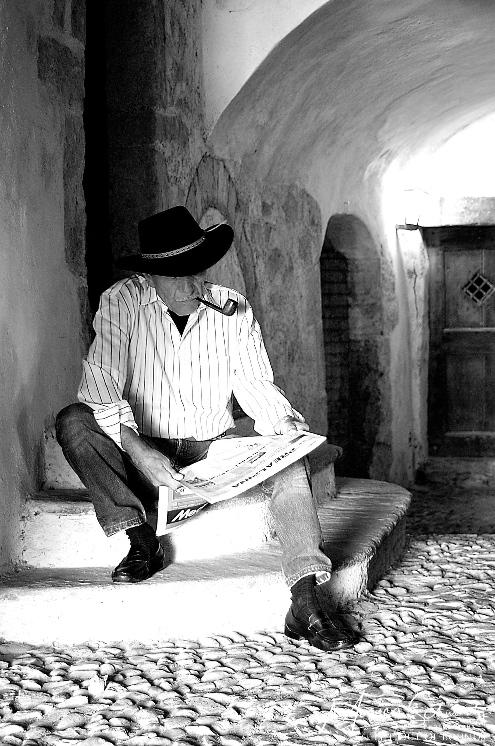 Portrait-of-Italian-man-smoking-a-pipe-and-reading-newspaper-in-medieval-village-setting